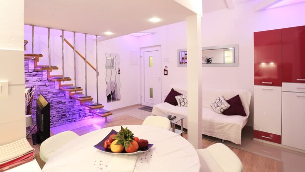 Una sala de estar moderna con una escalera, un comedor con un frutero y una cocina con armarios rojos.