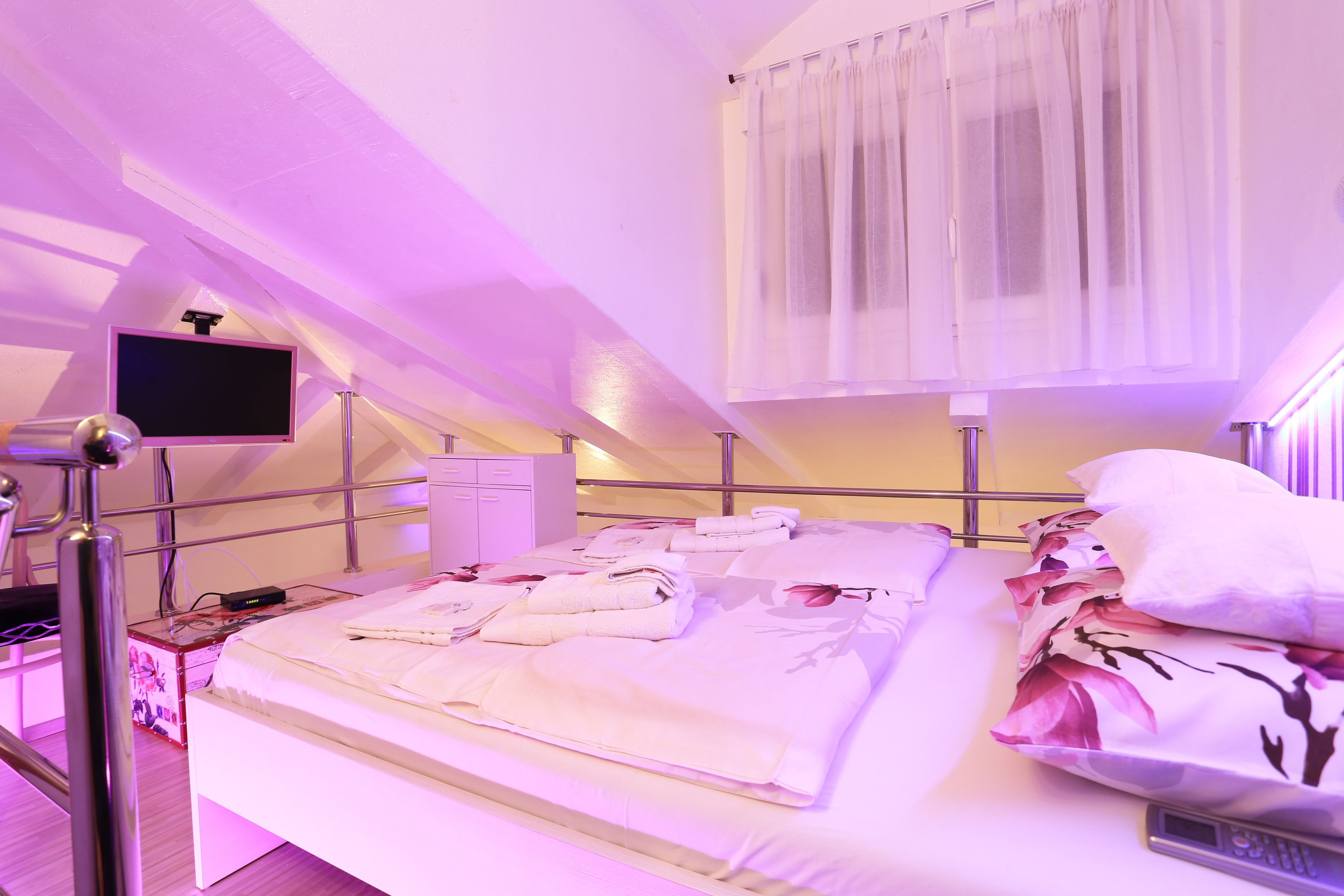A neatly made bed with towels, a bedside table with a lamp, and a TV mounted on the wall.