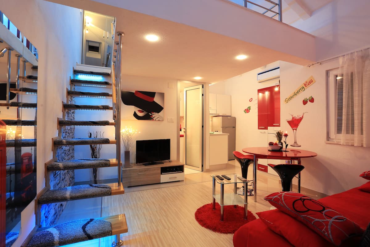 A modern living room with a staircase, a flat-screen TV, a dining area, and a kitchen.
