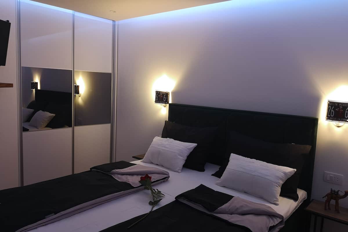 A modern bedroom with a bed, bedside lamps, a mirror, and a small nightstand with a figurine.