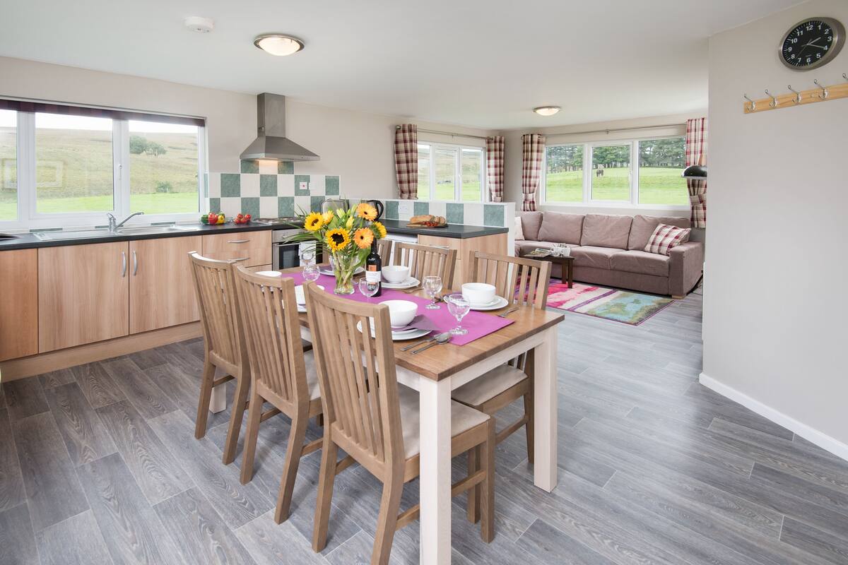 A modern kitchen with wooden cabinets, a dining table set for four, and a view of the outdoors.