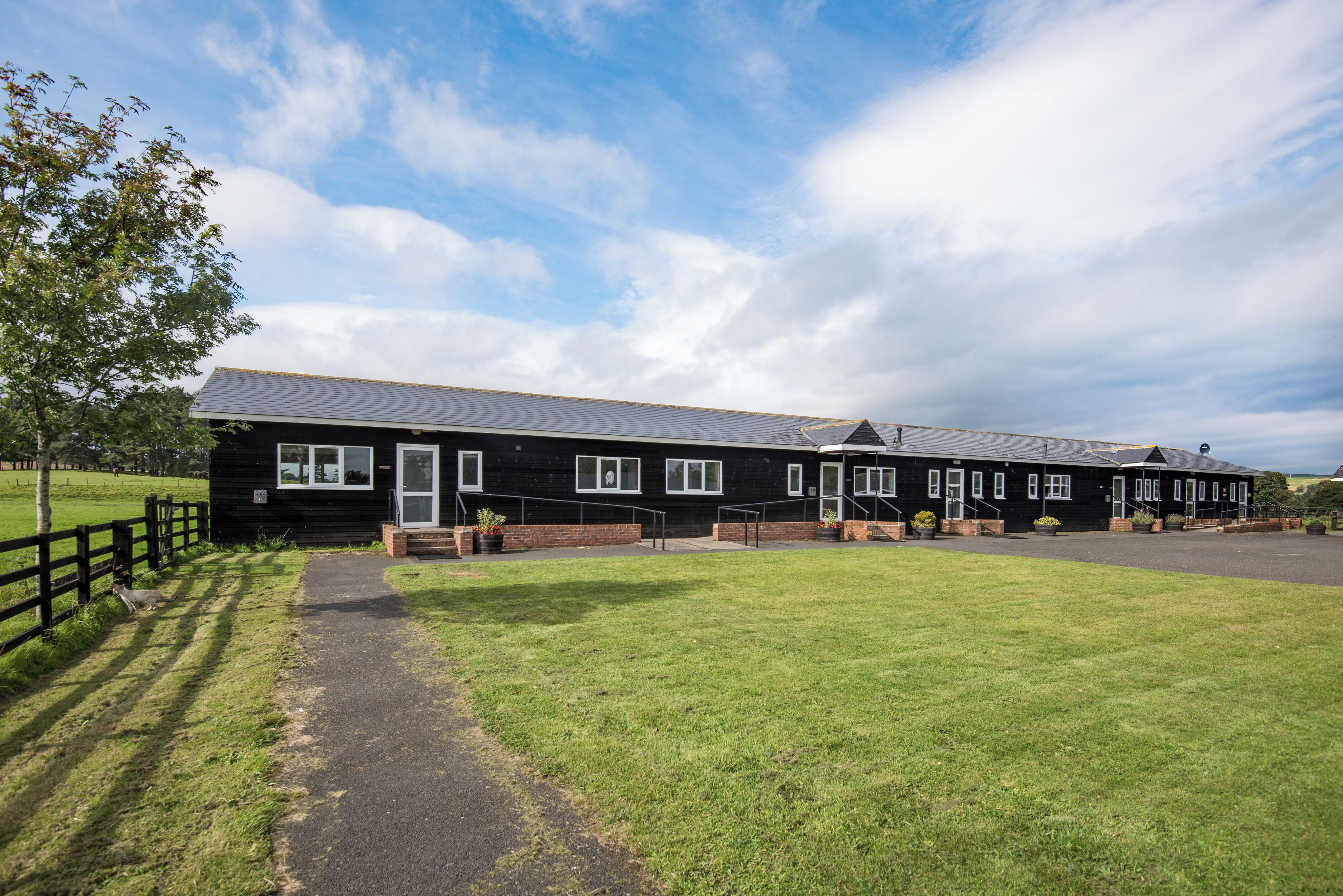 A row of black buildings with a paved walkway leading to them, surrounded by a grassy area.