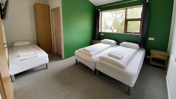 Une chambre avec deux lits simples, une armoire en bois, une petite table et une fenêtre avec des rideaux.