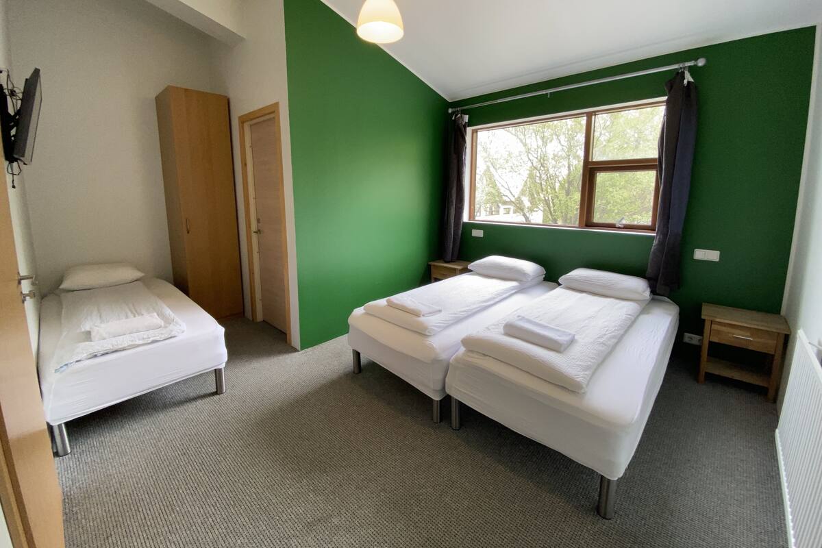 Ein Zimmer mit zwei Einzelbetten, einem Holzschrank, einem kleinen Tisch und einem Fenster mit Vorhängen.