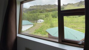 Een raam met uitzicht op een landelijk landschap, met groene velden en een klein gebouw met een groen dak.