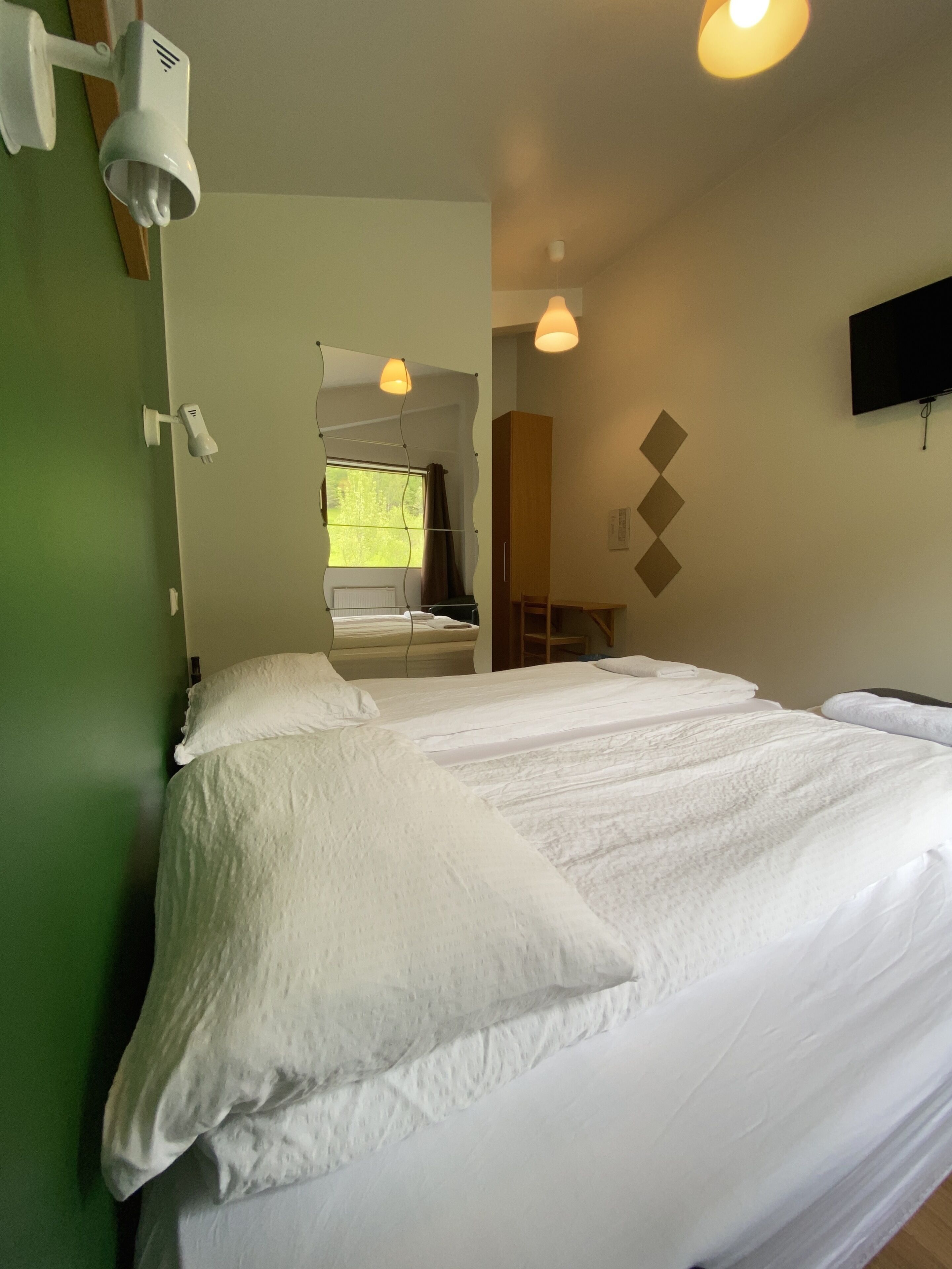 A hotel room with a large bed, a desk, a chair, a TV mounted on the wall, and a window with curtains.