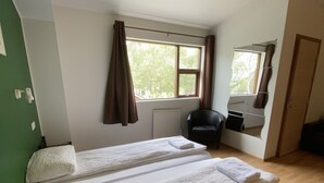 Een kamer met twee bedden, een radiator, een stoel en een raam met gordijnen.
