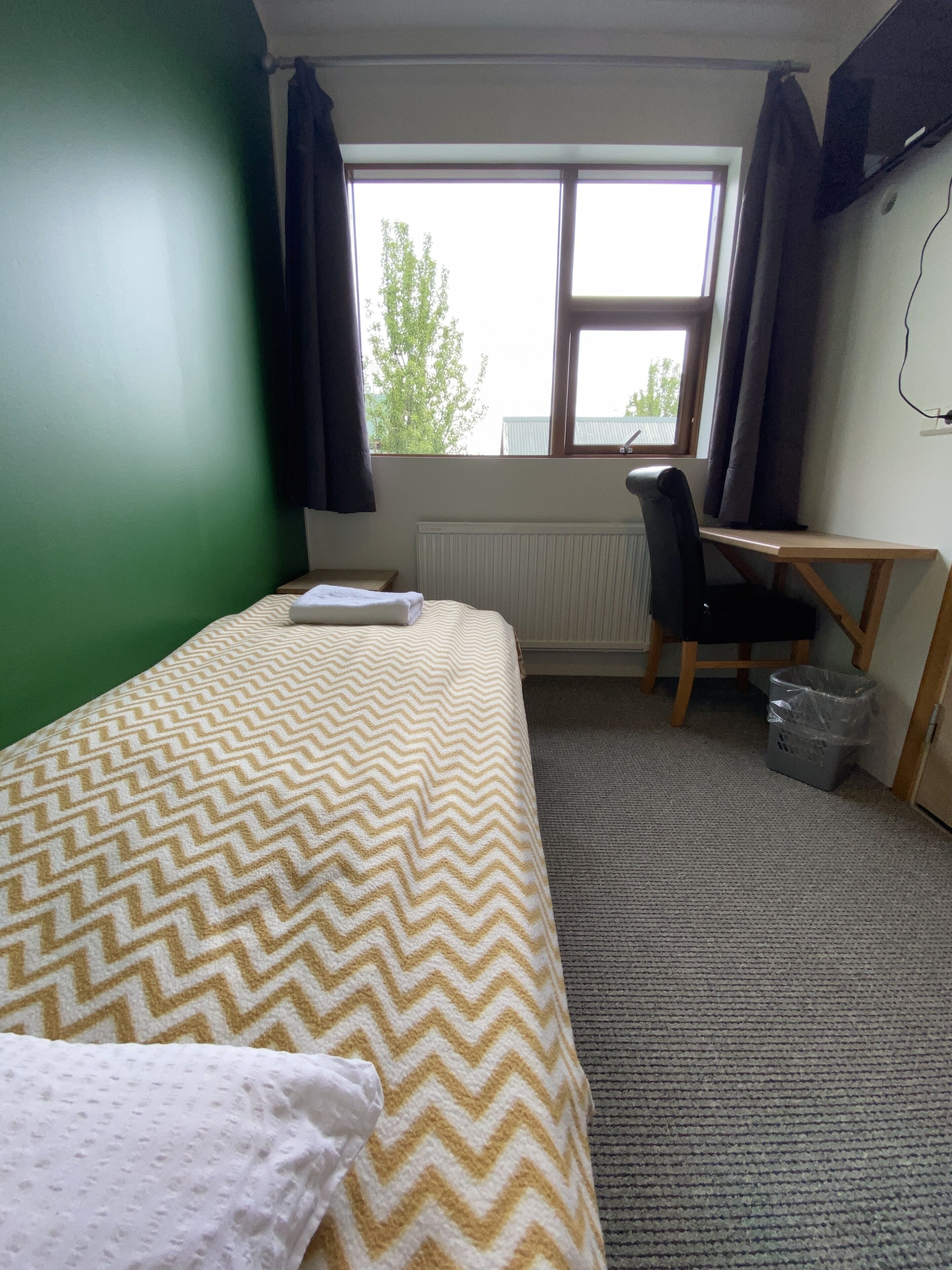 Una habitación con cama, escritorio, silla, radiador y ventana con cortinas.