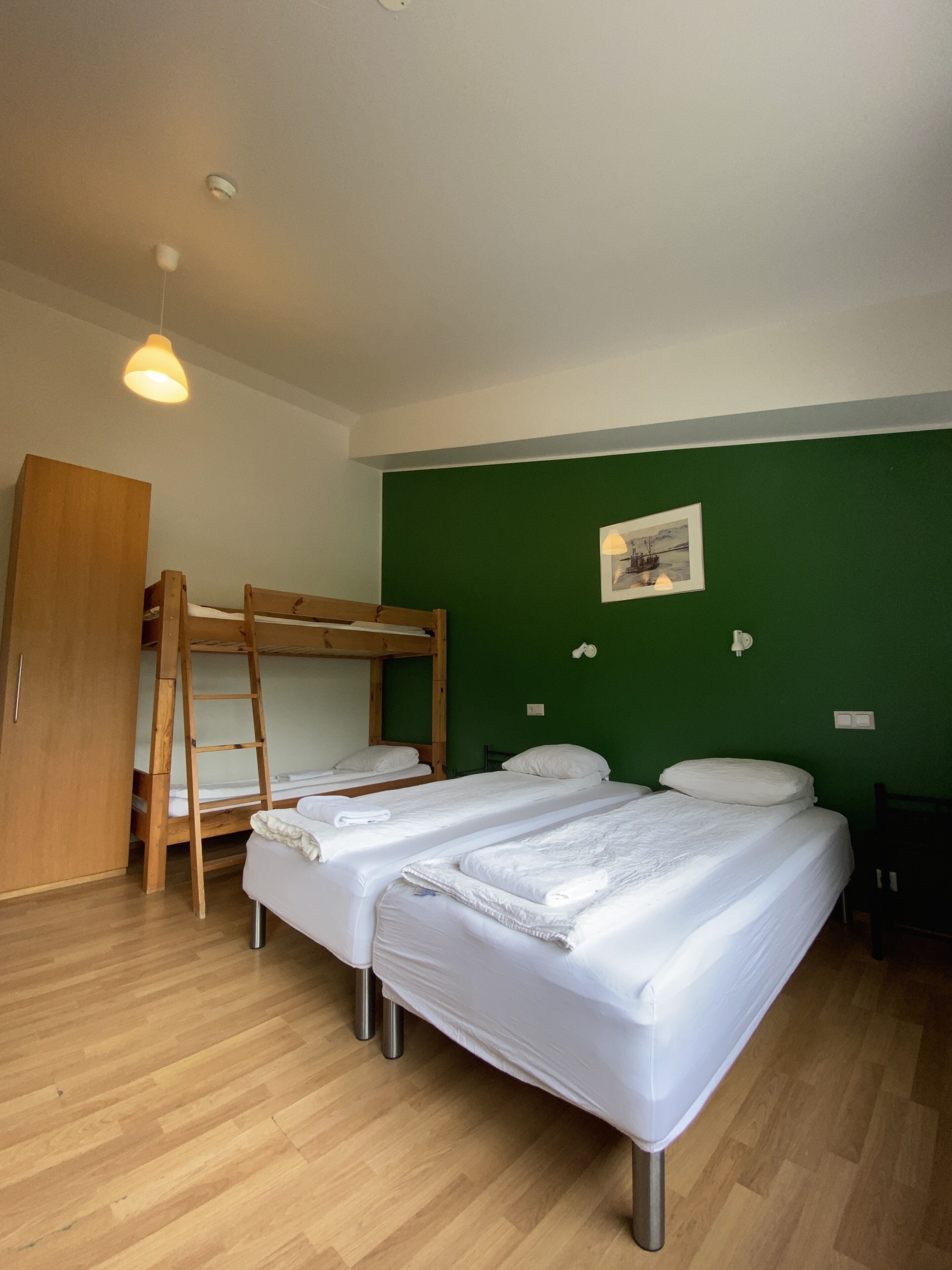 Una habitación con dos literas, un armario de madera, una escalera, una pared verde y una lámpara en el techo.