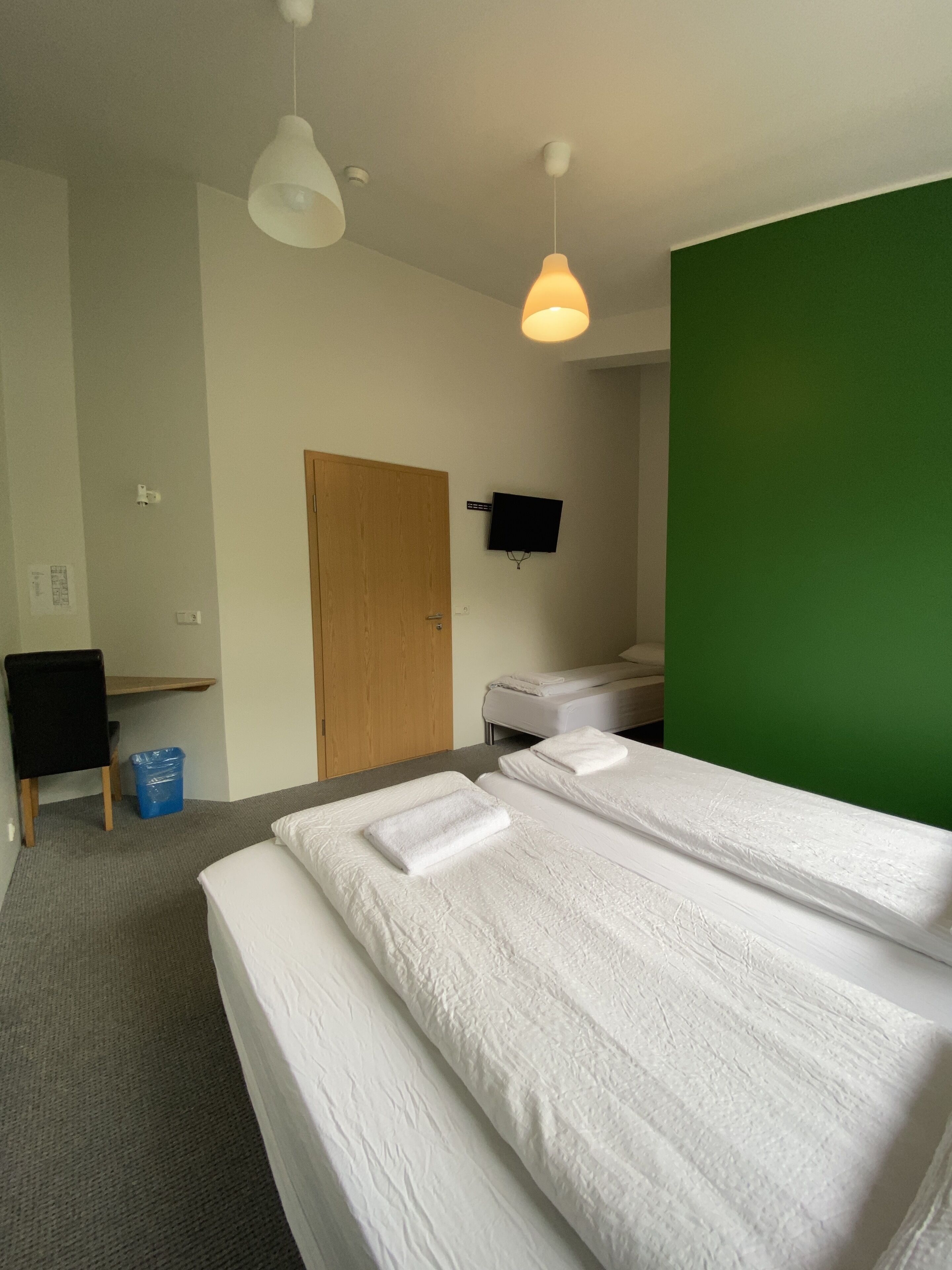 A hotel room with two beds, a desk, a chair, a television, and a green accent wall.