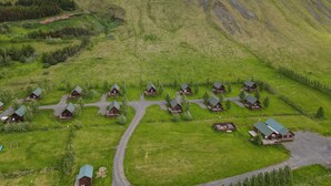 Un ensemble de chalets en rondins, coiffés de toits verts, disposés en arc de cercle autour d’une route centrale, le tout se dressant sur un fond de montagnes escarpées et d’un paysage verdoyant.