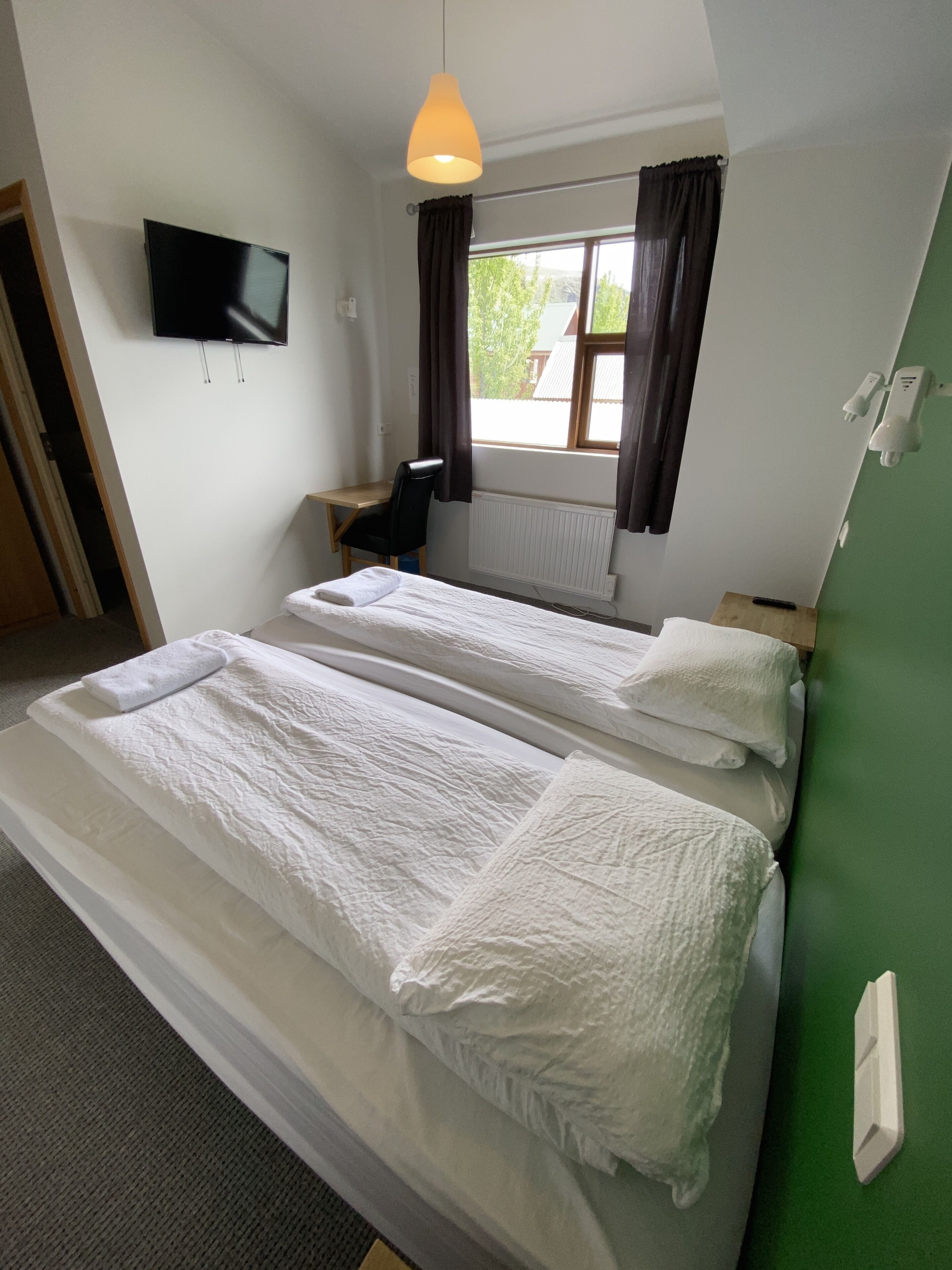 A hotel room with two beds, a desk, a chair, a TV, and a window with curtains.