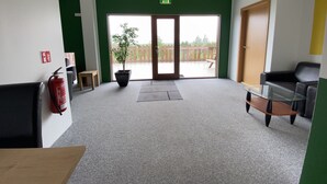 Een ruime lobby met een groene accentmuur, een brandblusser, een kamerplant, een glazen tafel en een houten bank.