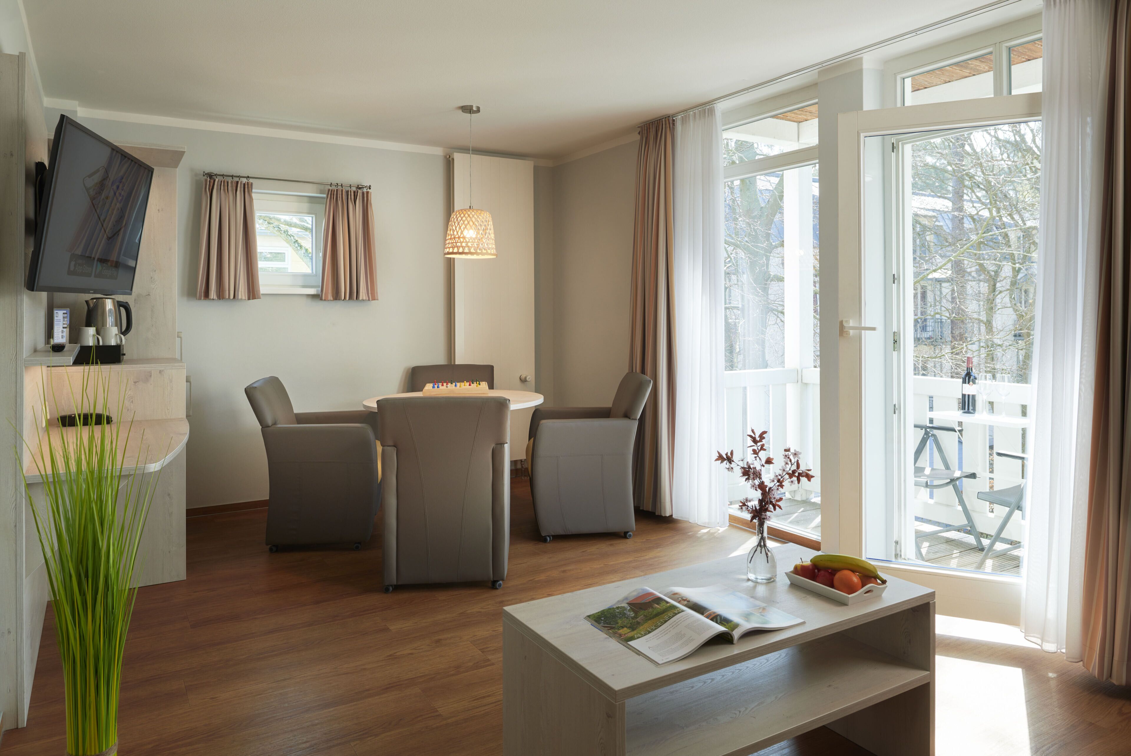 A modern living room with a flat-screen TV, a coffee maker, and a dining area with a table and chairs.