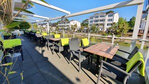 Un patio al aire libre con mesas y sillas, una estructura de pérgola y vistas a edificios residenciales al fondo.