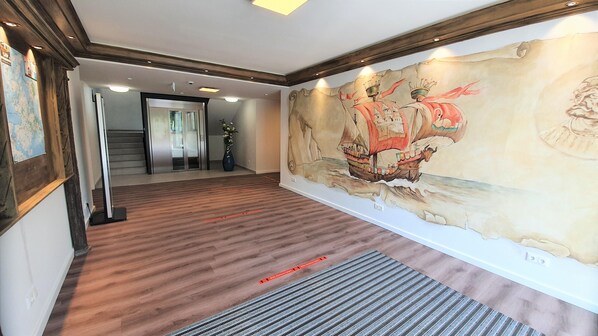A hallway with a wooden floor, a large mural of a ship, and a staircase with glass doors.