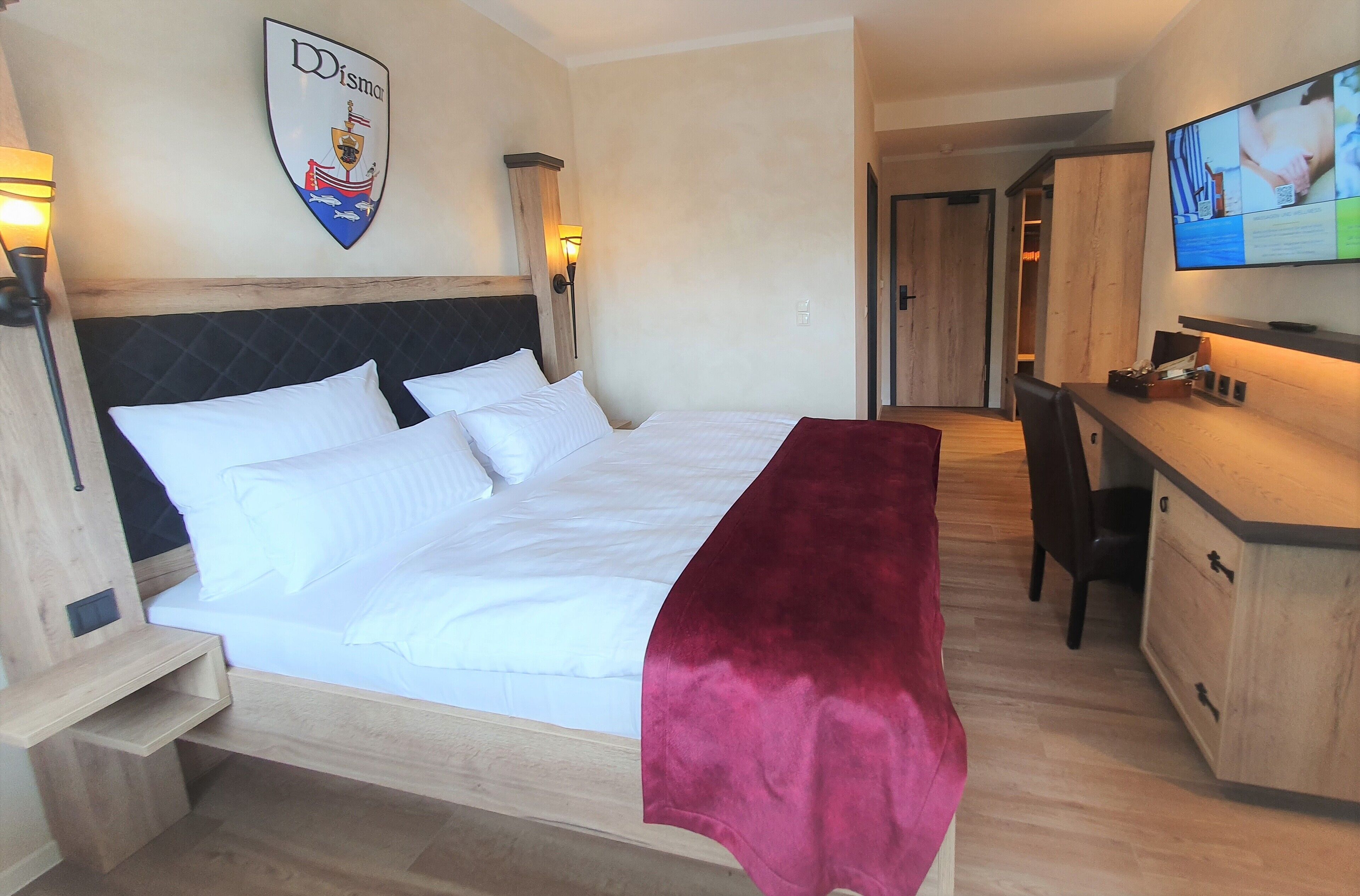 Ein Hotelzimmer mit Bett, Schreibtisch, Stuhl, Fernseher und Kleiderhaken.