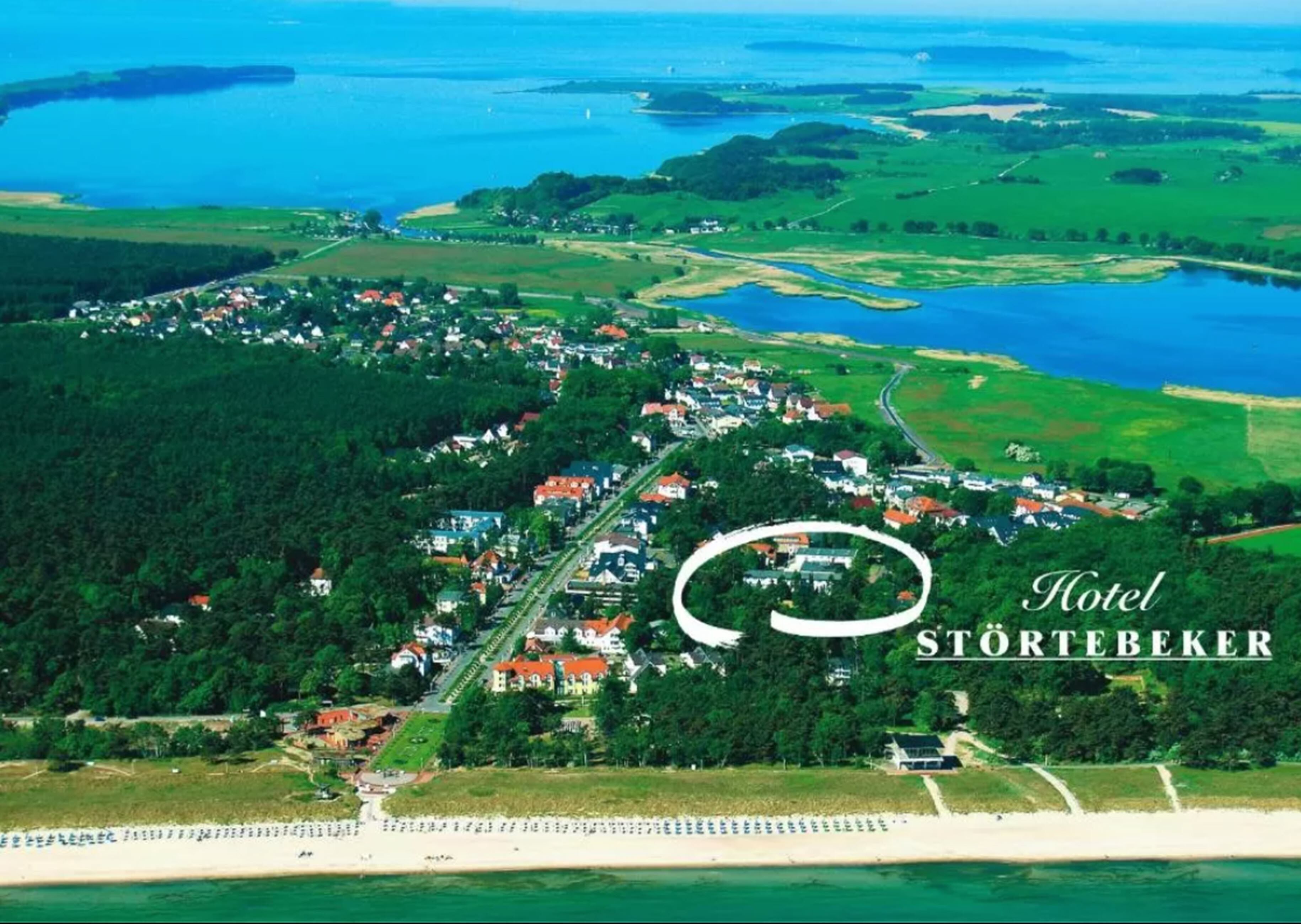 An aerial view of Hotel Störtebeker, surrounded by lush greenery and a coastal area.