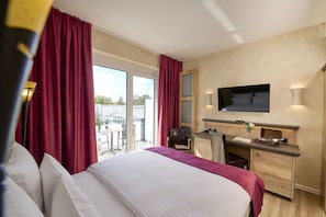 A hotel room with a bed, desk, TV, and a view of the outdoors.