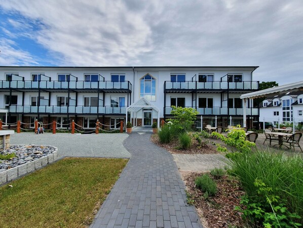 A hotel with a central entrance, outdoor seating, and a garden area.