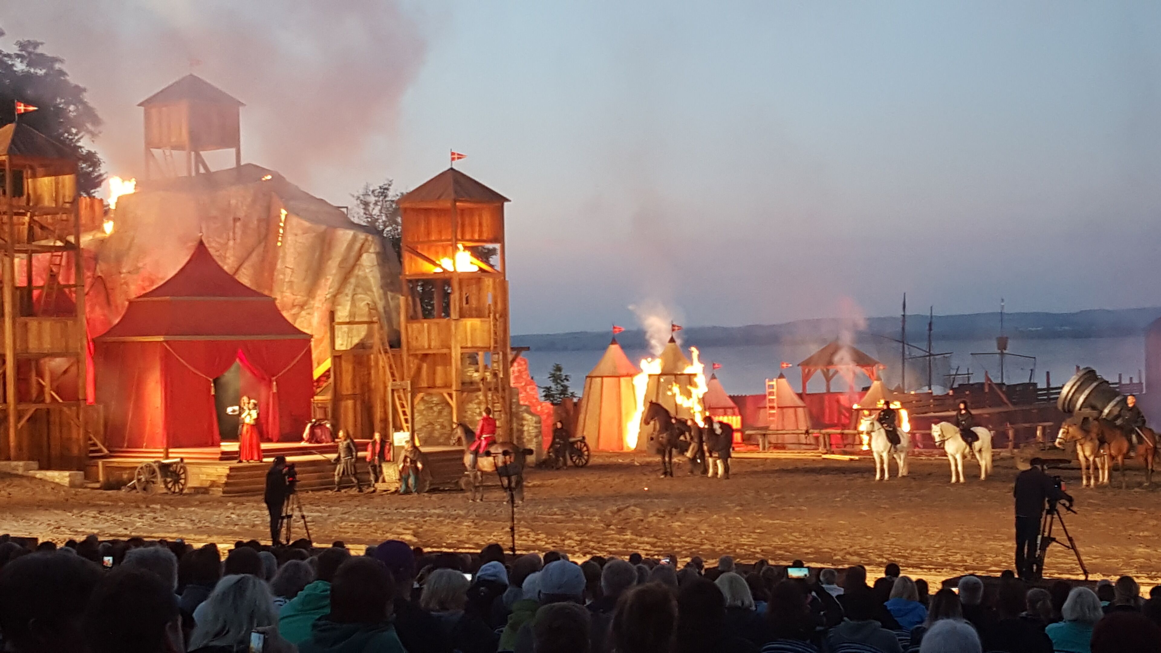 A medieval-themed outdoor event with wooden structures, horses, and performers.