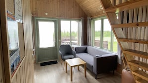 Une pièce avec un plafond en bois, un canapé, une table et une chaise. Il y a des fenêtres et une vue sur l’extérieur.