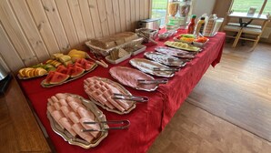 Une table de buffet proposant divers plats et accompagnements, installée dans une pièce aux murs en bois et offrant une vue sur l’extérieur.