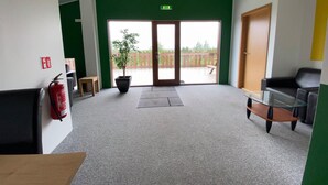 Un hall d’entrée spacieux avec un mur d’accent vert, un extincteur, une plante en pot et une table en verre.
