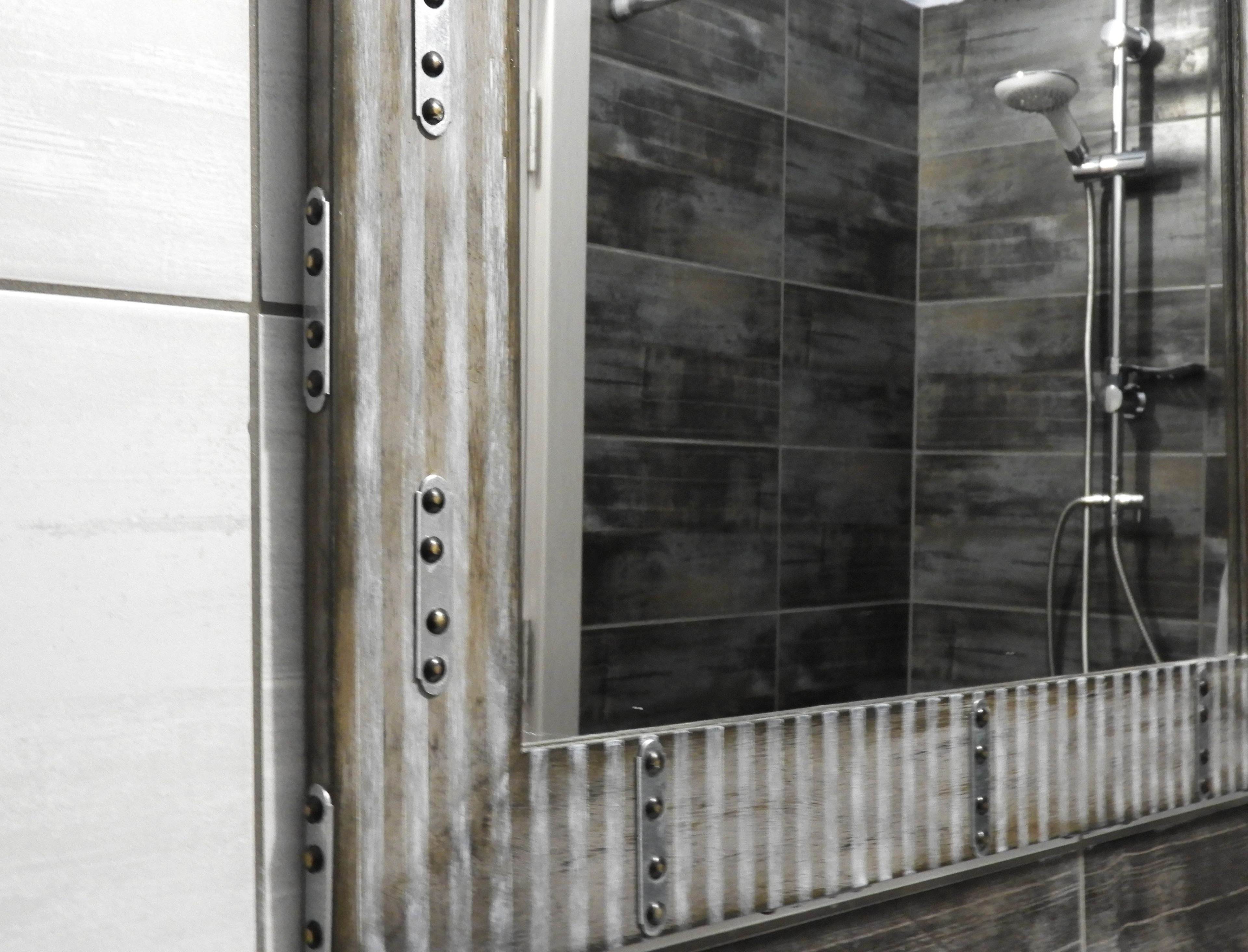 Un baño con un espejo grande, paredes de azulejos oscuros y una ducha.