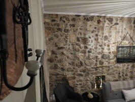 A room with a stone wall, a sofa, a small table with a vase, and a painting on the wall.