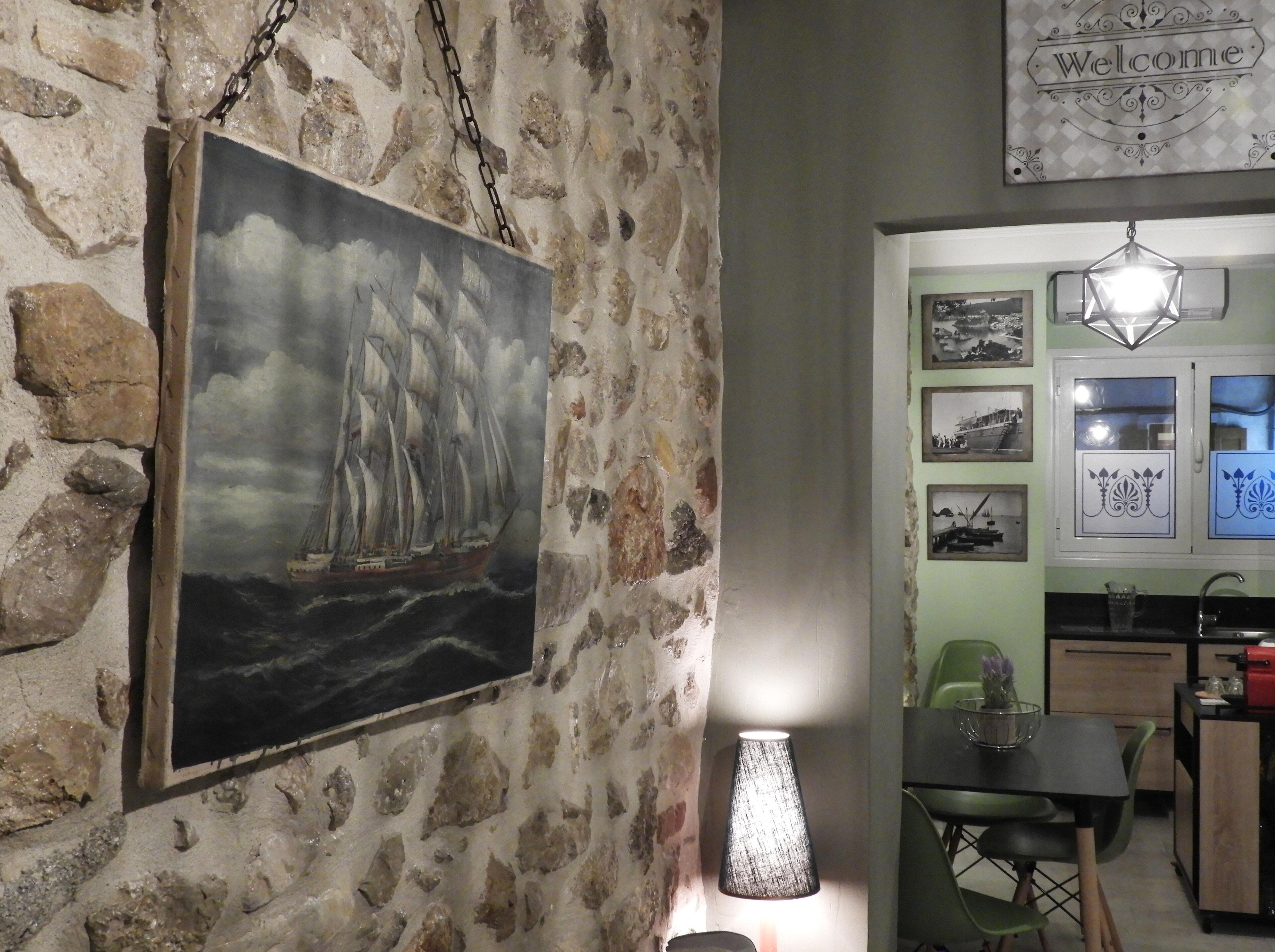 Una habitación con pared de piedra, un cuadro de barco, una mesa con sillas y un cartel de 'Welcome'.