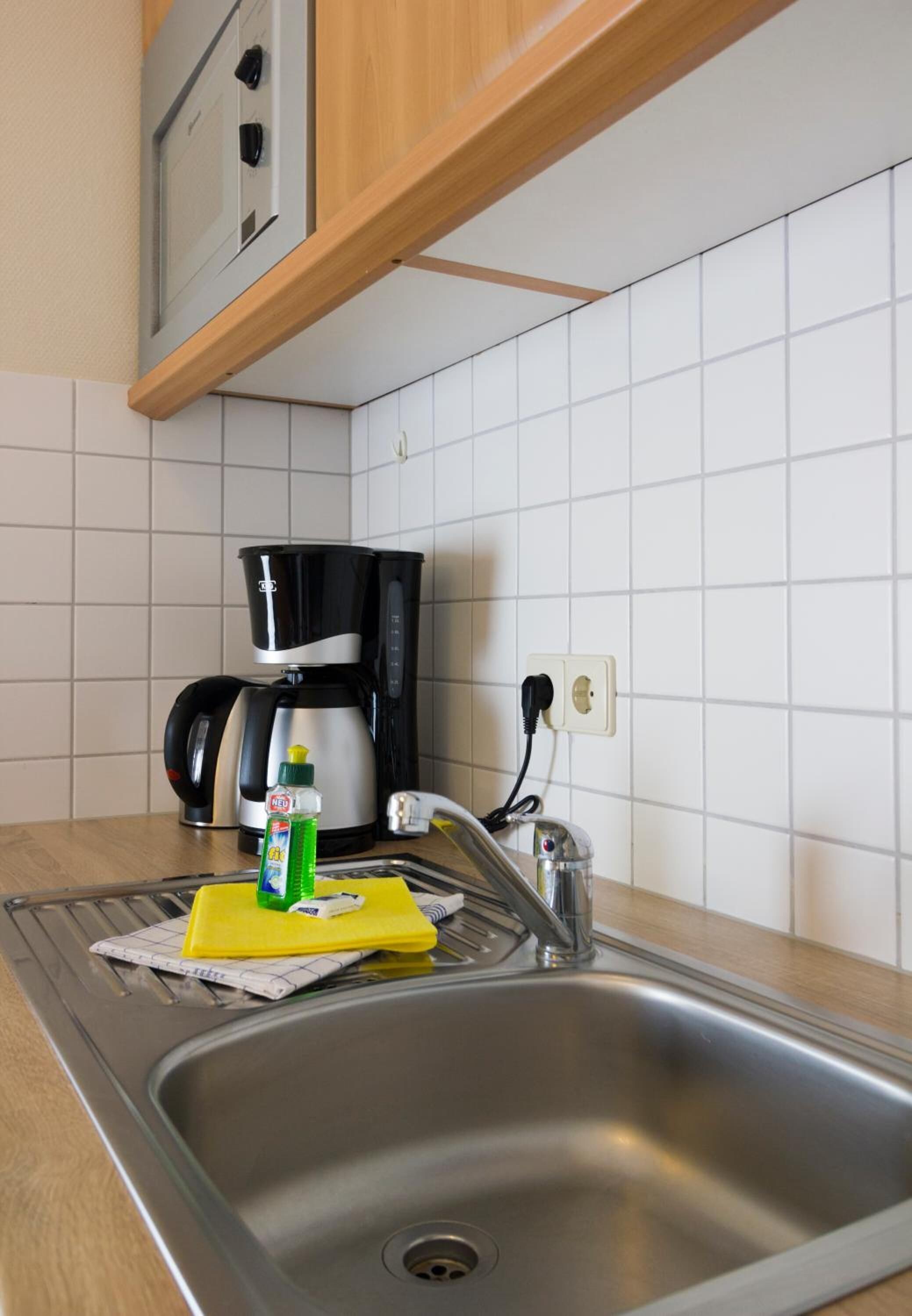 A kitchen with a stainless steel sink, a coffee maker, and a bottle of dish soap on the counter.