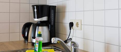 A kitchen with a stainless steel sink, a coffee maker, and a bottle of dish soap on the counter.