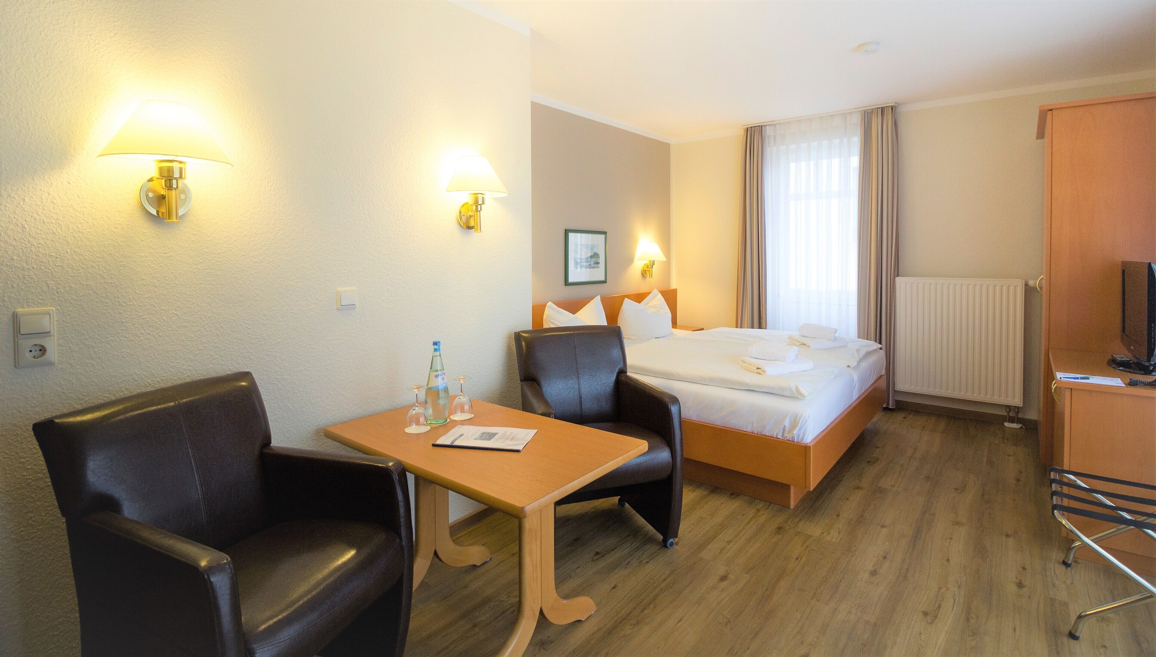 Une chambre d’hôtel avec un lit, deux chaises, une table, un téléviseur et une fenêtre avec des rideaux.