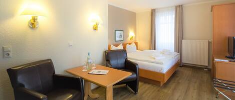 Une chambre d’hôtel avec un lit, deux chaises, une table, un téléviseur et une fenêtre avec des rideaux.