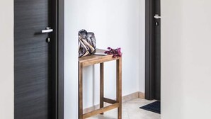 A hallway with two dark doors, a small wooden table with a bag and flowers, and a light switch on the wall. - La Medusa (Sant'Anna Arresi)