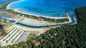An aerial view of a coastal area with a marina, beach, and surrounding forested hills. - La Medusa (Sant'Anna Arresi)