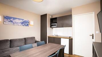 Een kleine keuken met een magnetron, een spoelbak en een eethoek met een tafel en stoelen.