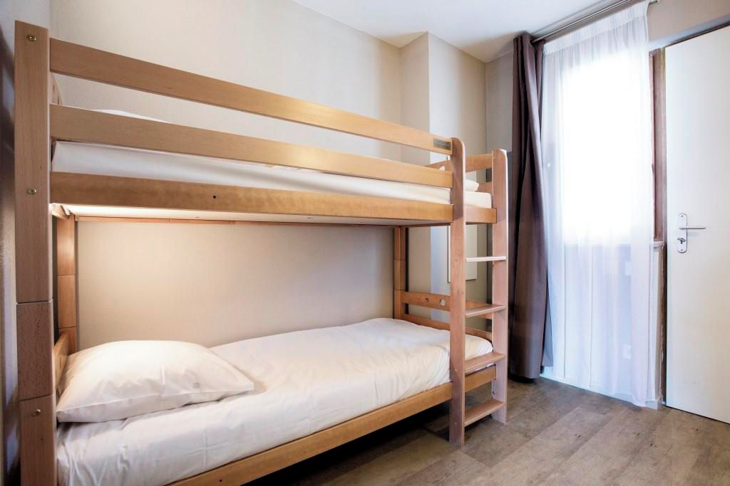 Dormitorio con literas de madera, colchón blanco y puerta con cortinas.