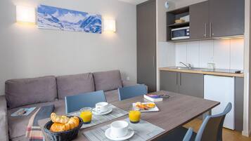 Een moderne hotelkamer met een ontbijt gedekte eettafel, een bank en een kitchenette met een magnetron en een spoelbak.