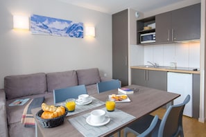 A modern hotel room with a dining table set for breakfast, a sofa, and a kitchen area with a microwave and sink. - Sowell Residences Pra Loup (Uvernet-Fours)