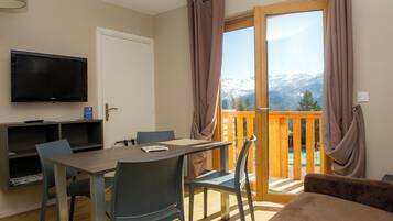 A room with a dining table, chairs, a TV, and a view of mountains through a large window.