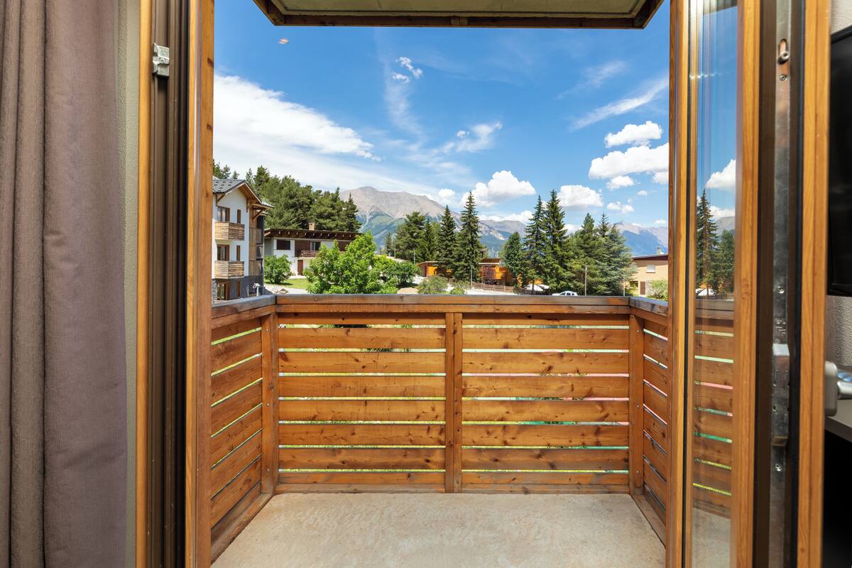 A wooden balcony with a view of mountains and buildings.