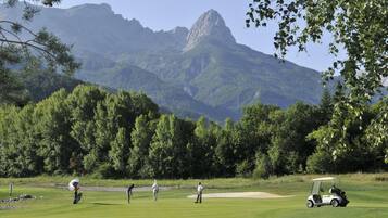 Campo de golf con montañas al fondo, un carrito de golf y jugadores en movimiento.