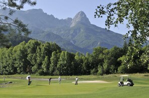 A golf course with a mountainous backdrop, a golf cart, and players in action. - Sowell Residences Pra Loup (Uvernet-Fours)