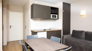 Una cocina compacta con microondas, armarios y un comedor con sillas.