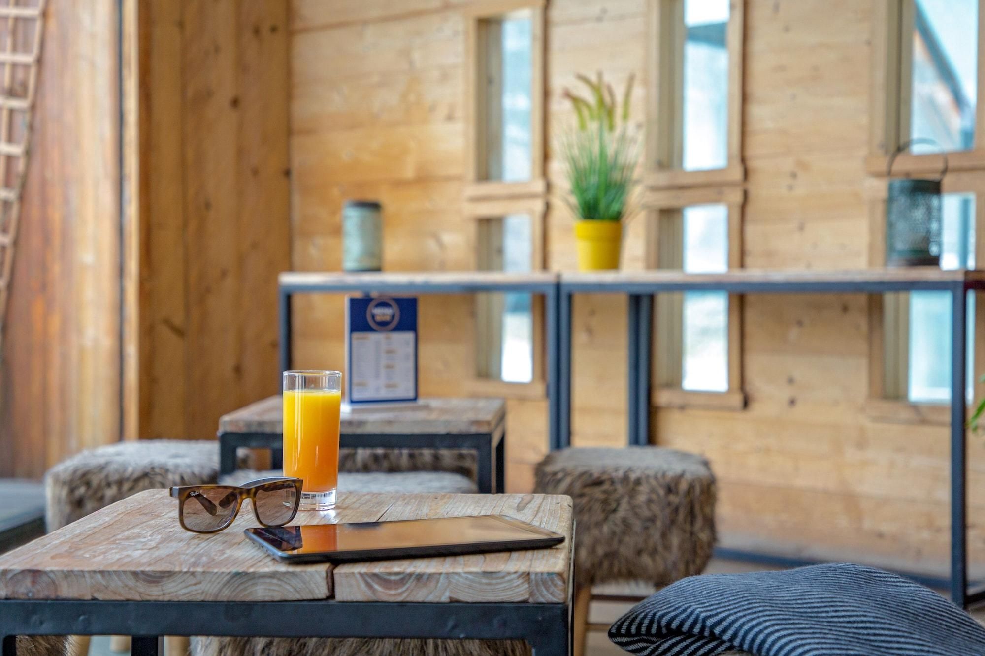 Un interior de madera con una mesa que sostiene un vaso de zumo de naranja, unas gafas de sol y un teléfono inteligente.