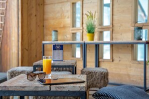 A wooden interior with a table holding a glass of orange juice, a pair of sunglasses, and a smartphone. - Sowell Residences Pra Loup (Uvernet-Fours)