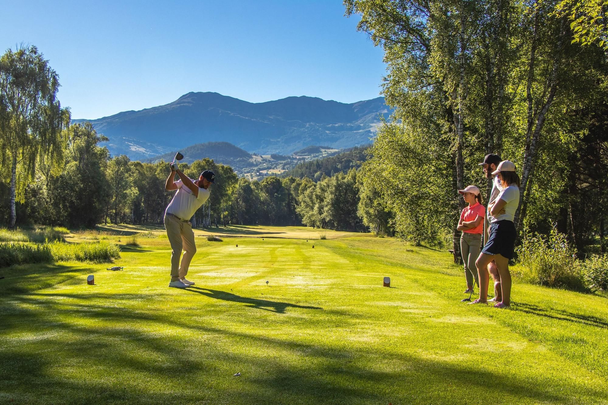 Un parcours de golf avec une chaîne de montagnes en arrière-plan, des arbres et un ciel dégagé.