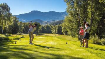 Un parcours de golf avec une chaîne de montagnes en arrière-plan, des arbres et un ciel dégagé.